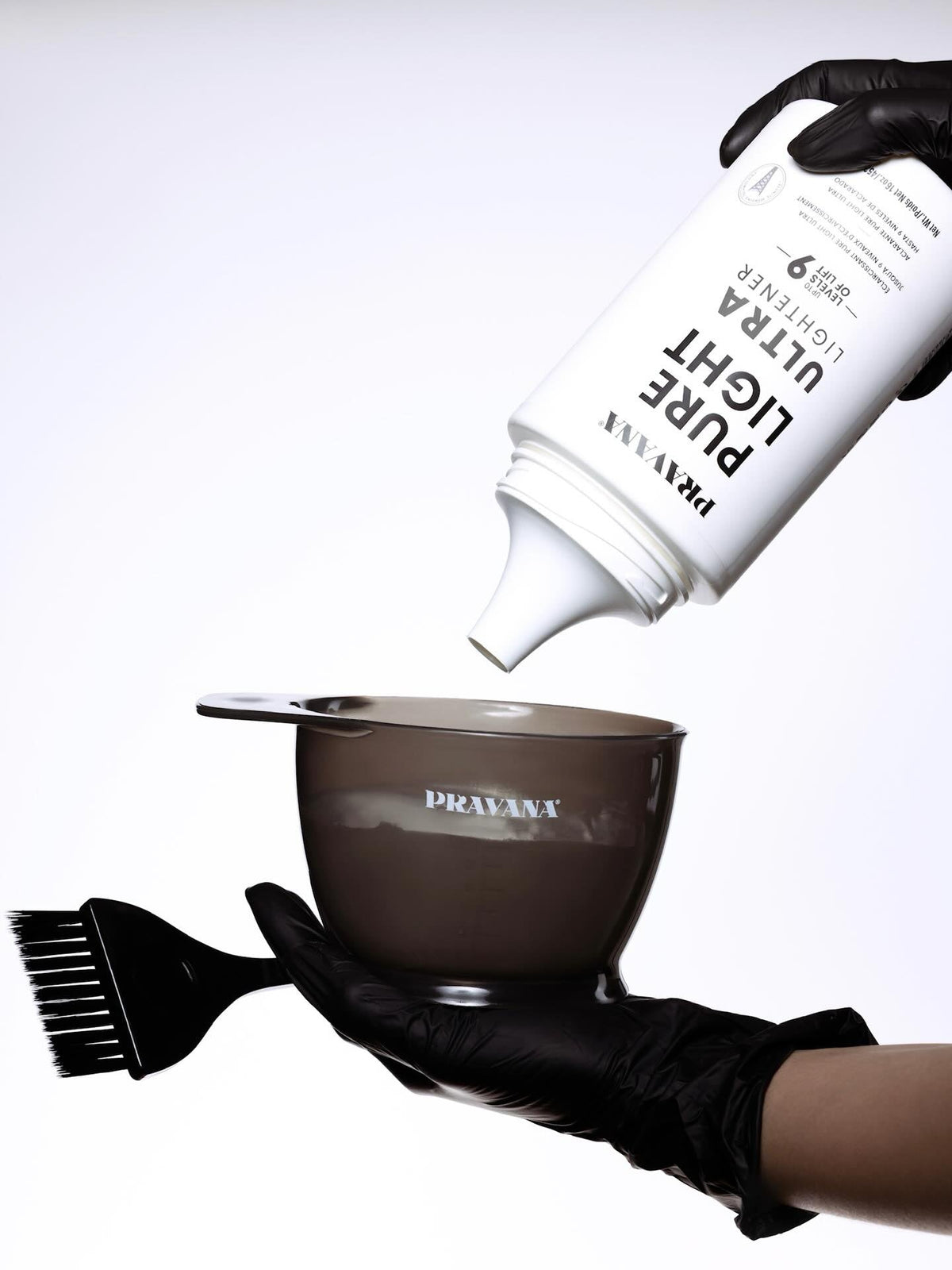 Pravana Colouring Bowl — in use, gloved hand dispensing lightener into the smoke-grey bowl with measuring scale