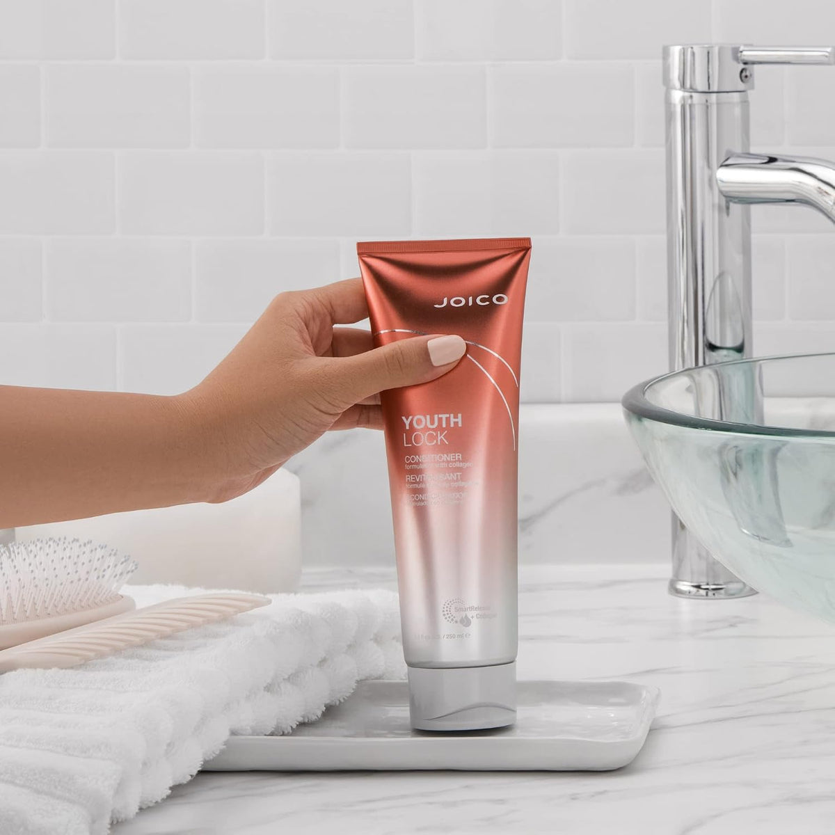 Joico YouthLock Conditioner — conditioner tube held in hand at a bathroom basin, lifestyle shot