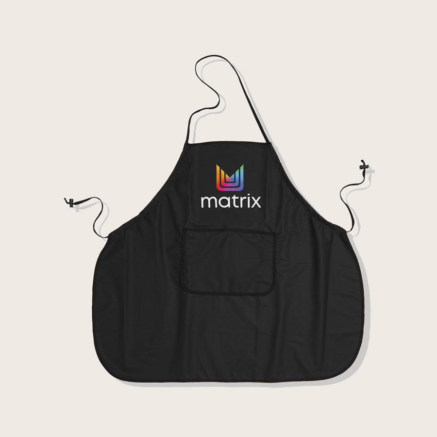 Matrix Salon Apron #34 — black salon bib apron with a neck loop, waist ties, a front pocket and the Matrix logo at the chest, shown flat on a plain background