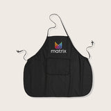 Matrix Salon Apron #34 — black salon bib apron with a neck loop, waist ties, a front pocket and the Matrix logo at the chest, shown flat on a plain background