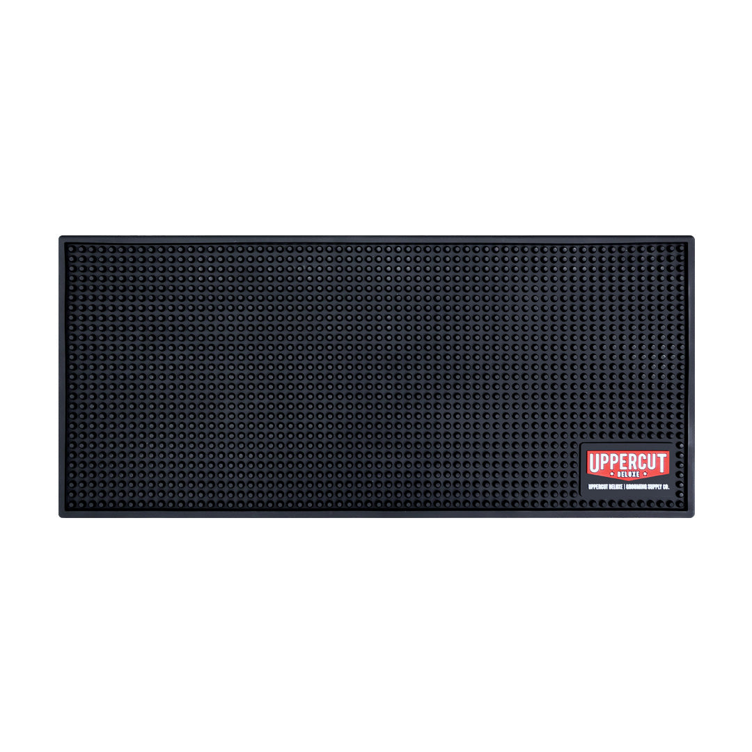 Uppercut Deluxe Barber Station Mat — black studded non-slip counter mat with the red Uppercut Deluxe Grooming Supply Co. badge, plain white background