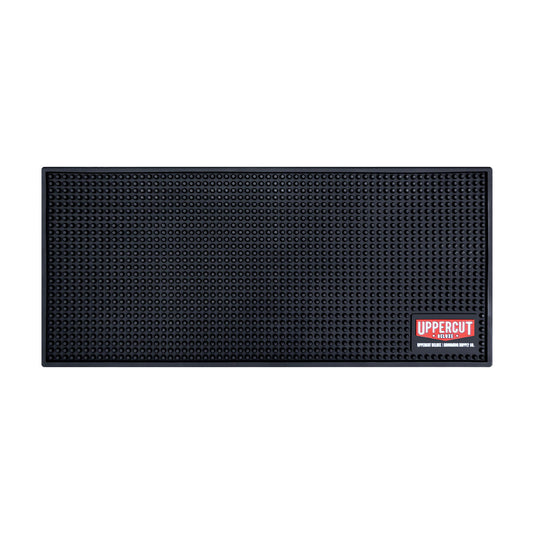 Uppercut Deluxe Barber Station Mat — black studded non-slip counter mat with the red Uppercut Deluxe Grooming Supply Co. badge, plain white background