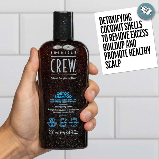 American Crew Detox Shampoo — hand holding the 250 ml bottle against white tiles beside a card about detoxifying coconut shells
