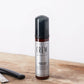 American Crew Beard Foam Cleanser 70ml — 70 ml foam cleanser pump bottle standing on a wooden barber counter beside a straight razor