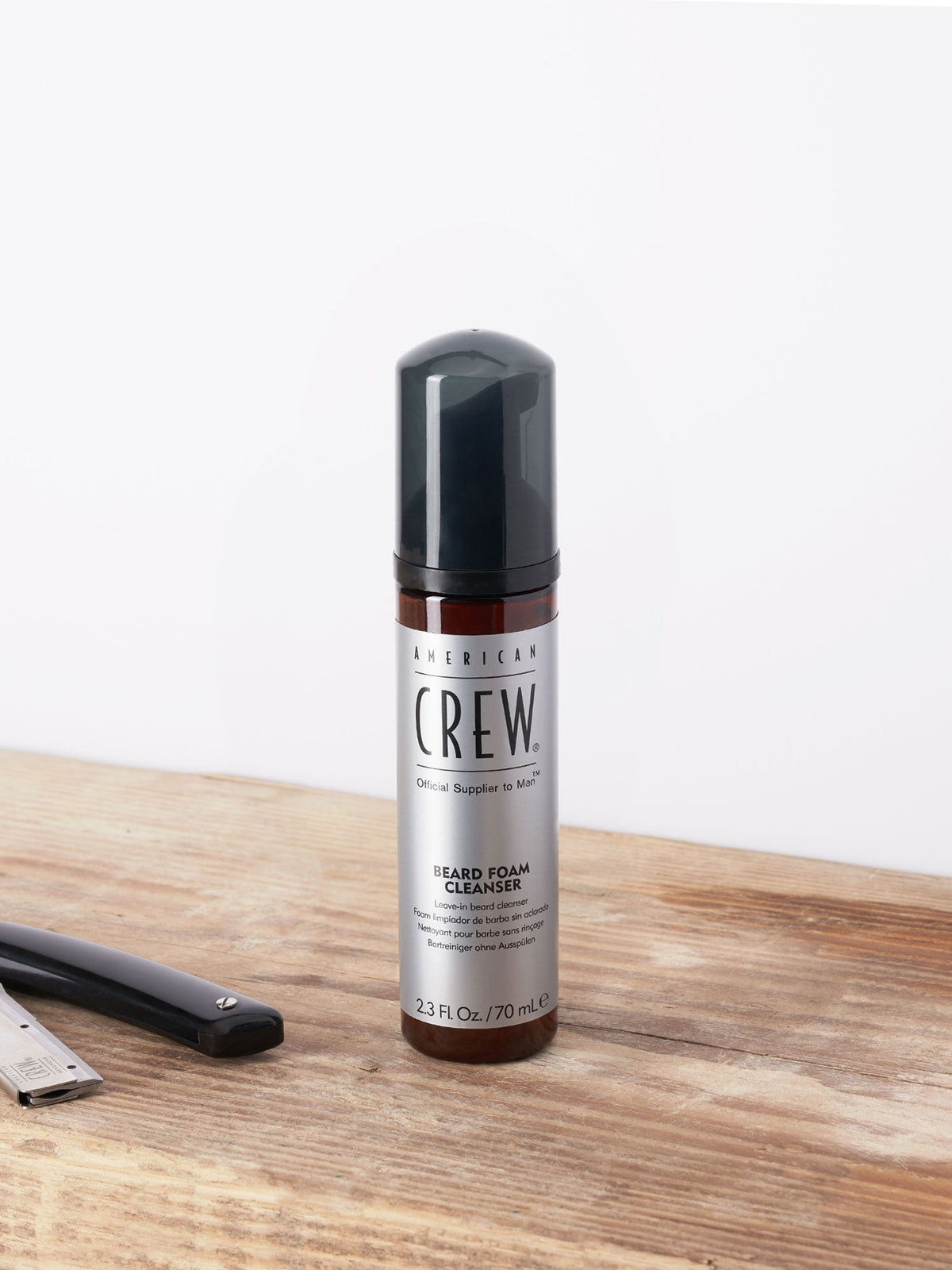 American Crew Beard Foam Cleanser 70ml — 70 ml foam cleanser pump bottle standing on a wooden barber counter beside a straight razor