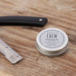 American Crew Moustache Wax — 15 g tin on a wooden barber counter beside a straight razor