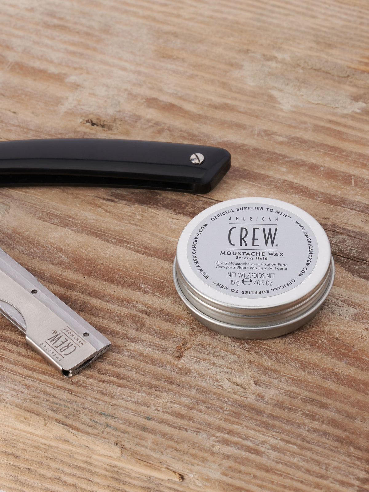 American Crew Moustache Wax — 15 g tin on a wooden barber counter beside a straight razor