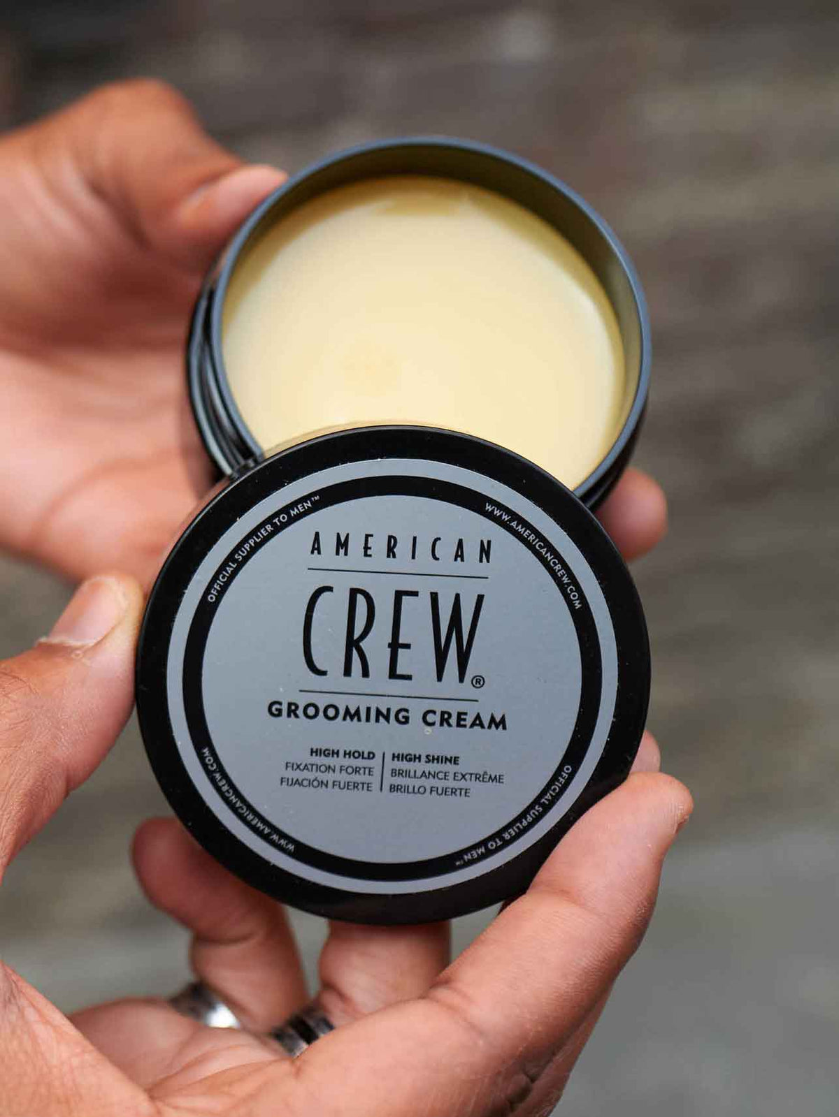 American Crew Grooming Cream — open puck held in a hand, showing the cream inside the tin