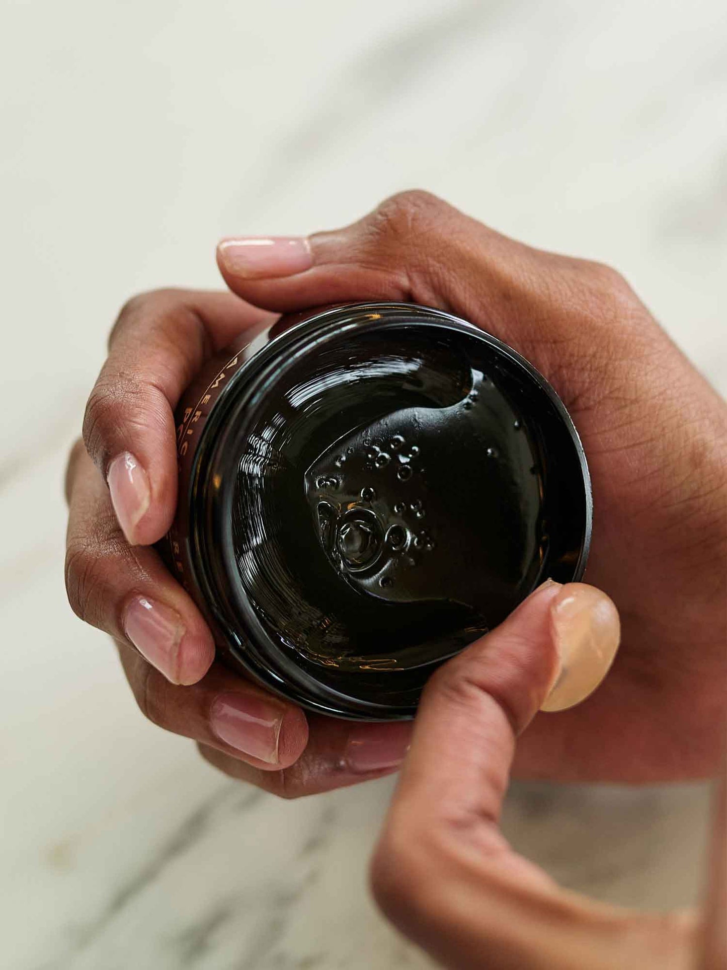 American Crew Pomade — open tub held in hand showing the glossy pomade texture